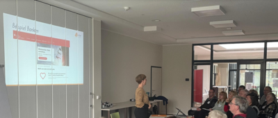 Referentin steht vor den Teilnehmenden, im Hintergrund ein Schaubild zum Thema Finanzierung